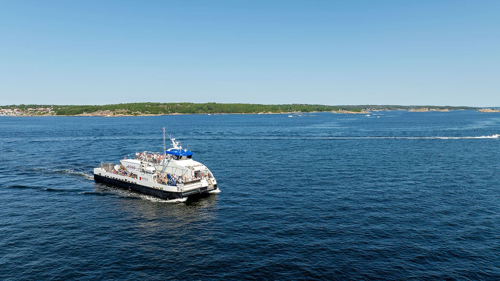 Ferge med passasjerer krysser det åpne havet mellom Hvalerøyene på en klar sommerdag.