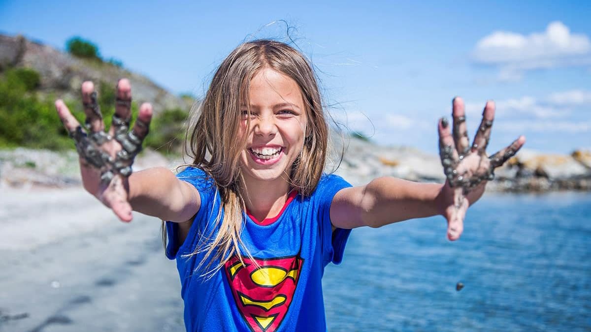 Smilende barn med gjørmete hender leker på stranden en sommerdag.