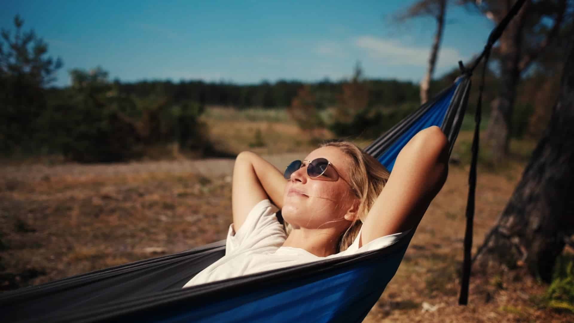 Kvinne ligger og slapper av i en blå hengekøye med solbriller.