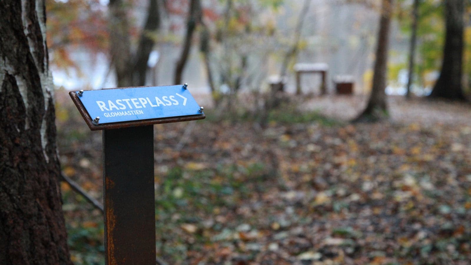 Nærbilde av blått skilt som peker mot rasteplass på Glommastien.