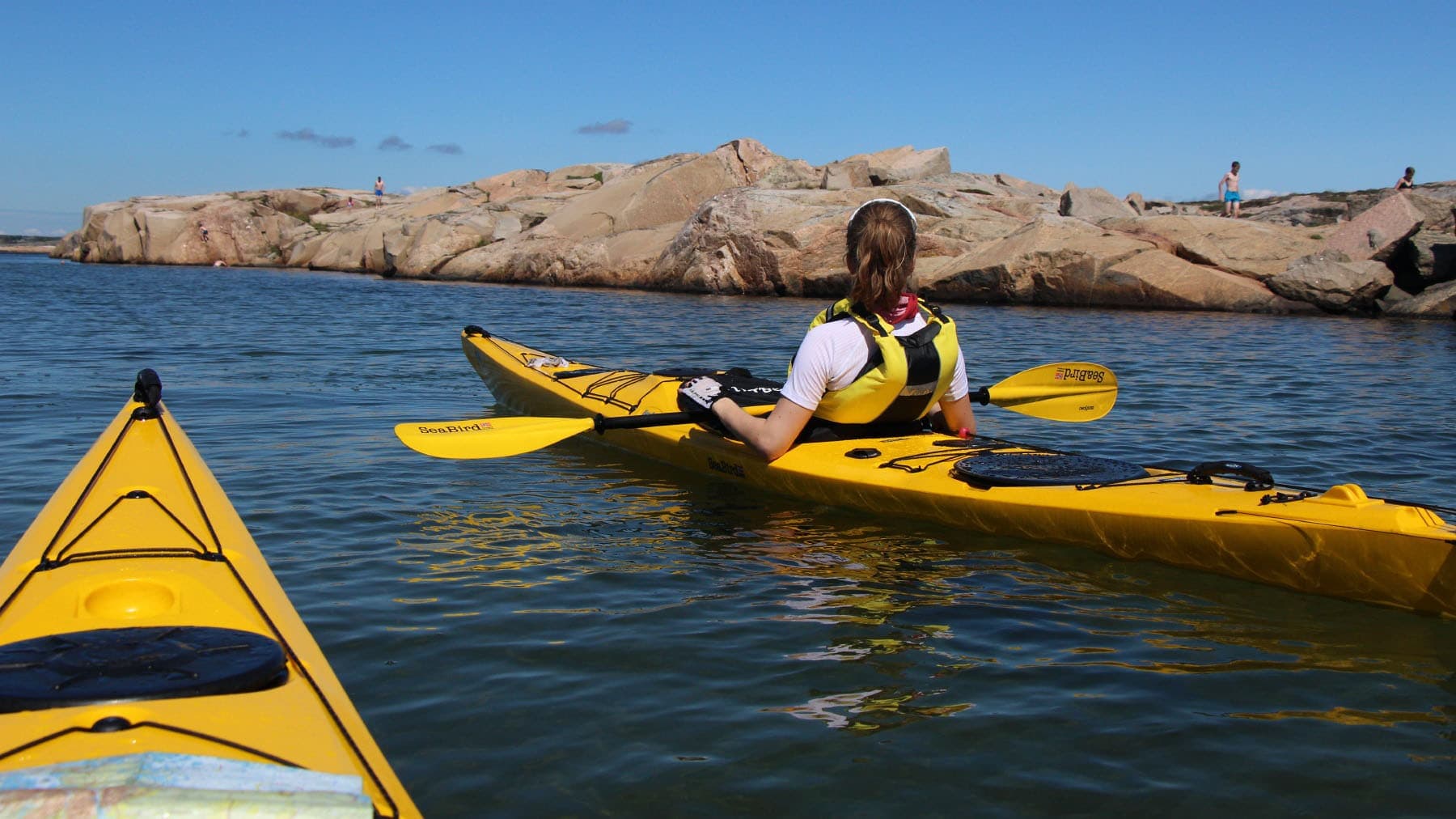 To kajakkpadlere ved svabergene i ytre skjærgård med klart blått vann.