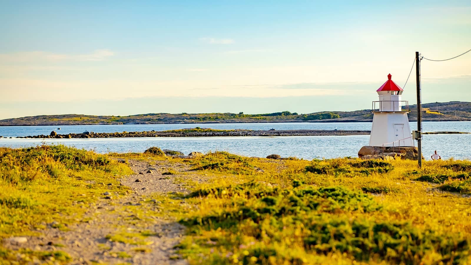Hvit fyrlykt med rød topp ved Pikesten på Brattestø, omgitt av svaberg og hav i gyllent ettermiddagslys.